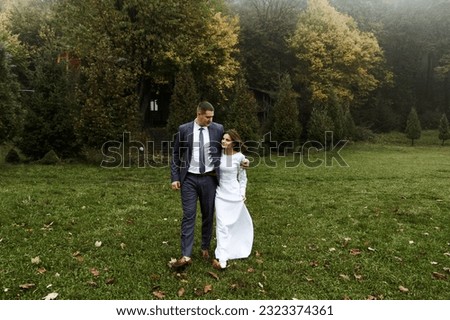 young wedding couple outdoors in the autumn season. autumn wedding day. height difference. the groom hugs the bride to him. the newlywed on the background of fog and fallen leaves