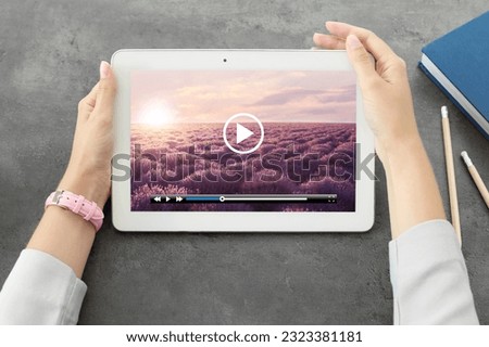 Woman watching video on tablet at grey desk, closeup