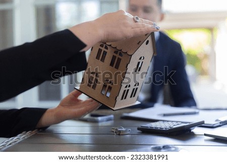 Female agent shows wooden model of house in agency office. Professional realtor talks with potential client about signing contract