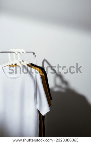 Blank white t-shirt mockup, template on white palstic hanger displayed on white cloths rack with yellow and black t-shirts