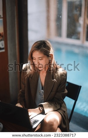 Young Asian business woman wearing suit using laptop in cafe. Happy smiling female professional working holding notebook . Royalty-Free Stock Photo #2323388717
