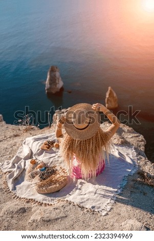 woman sea travel. photo of a beautiful woman with long blond hair in a pink shirt and denim shorts and a hat having a picnic on a hill overlooking the sea