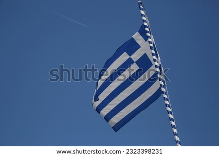 Greek flag on flagpole waving in the wind with clear blue sky behind Traditional colors of Greece: blue symbolizes the sky and the sea, white symbolizes the clouds and the waves.
