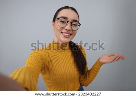 Smiling young woman taking selfie on grey background