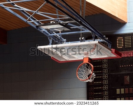 Folded  Basketball board and basket rim. Digital score board.  High power led light system Hoop red metal ring and white net under roof in school gym Royalty-Free Stock Photo #2323411265