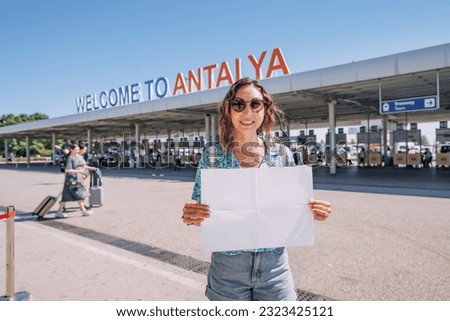 Girl with blank paper at the welcome to Antalya sign at the arrival international terminal of Airport with tourists. Huge tourist traffic concept