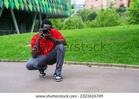Young black photographer taking pictures with a digital camera. with the camera looking through the lens in a park in Bilbao, in front of the Bilbao Arena, sports palace of Bilbao. Young black profess