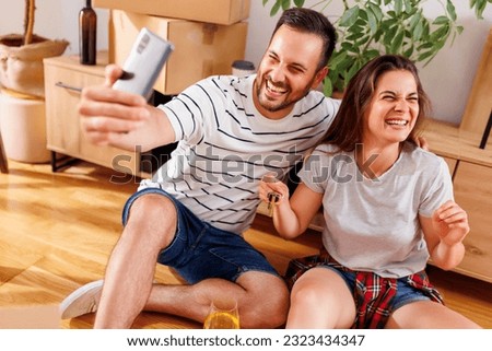Young couple in love moving in together in their new apartment, having fun taking selfies with apartment keys