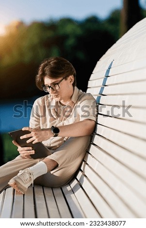 Young man sitting on a bench and using laptop. People, friendship, studying, lifestyle concept                               