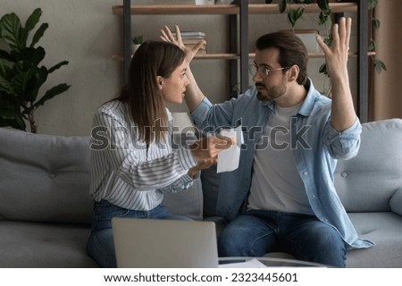 Stressed emotional young family couple arguing, blaming each other of overspending money, having financial problems, made mistakes in bills taxes payments, feeling depressed together at home. Royalty-Free Stock Photo #2323445601