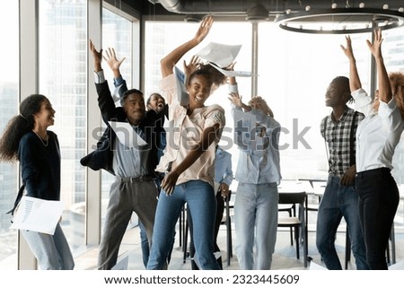 Overjoyed young african american female and male colleagues throwing papers in air, celebrating shared corporate success or goal achievement, enjoying carefree party time in modern office room. Royalty-Free Stock Photo #2323445609