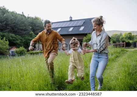 Family walking near their house with photovoltiacs panels on the roof. Royalty-Free Stock Photo #2323448587