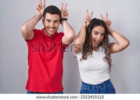 Young hispanic couple standing over isolated background posing funny and crazy with fingers on head as bunny ears, smiling cheerful 
