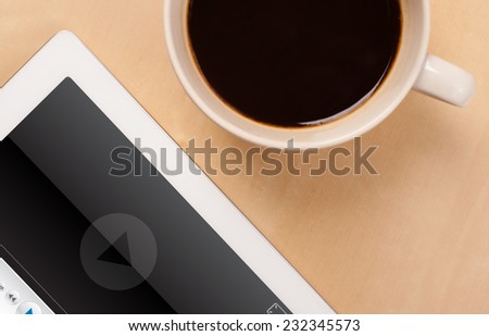 Workplace with tablet pc showing media player and a cup of coffee on a wooden work table close-up