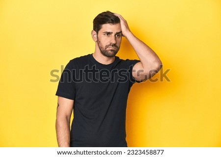 Caucasian man in black t-shirt, yellow studio backdrop tired and very sleepy keeping hand on head.