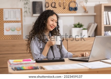 Asian woman holding cup enjoy favorite tea drink, morning beverage while sitting at working desk in modern living room before start work. Break, pause, daydreaming work life balance concept.