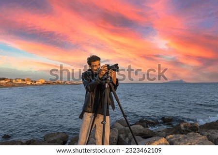 Conceptual photo of a photographer or videomaker who takes photographs by the sea to learn by directing actors. Videomaking and photography school with a model man