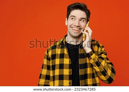 Young happy man he wear yellow checkered shirt black t-shirt talk speak on mobile cell phone conducting pleasant conversation isolated on plain red orange background studio portrait. Lifestyle concept