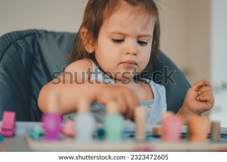Cute little girl sitting at table and playing with toys while spending time at home