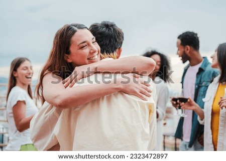 Happy young woman giving a hug to her boyfriend on a social festive party with their best friends. Affectionate couple embracing each other on a social gathering. Glad female greeting her husband
