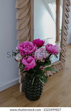 a vase with a bouquet of peonies stands on the floor next to a mirror  in a wooden frame