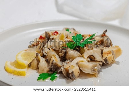 Rapana clam meat with oil, spices and greens. Healthy seafood is rich in omega. Marine decor, hard light, dark shadow, white plaster background, flat lay, close up Royalty-Free Stock Photo #2323515411