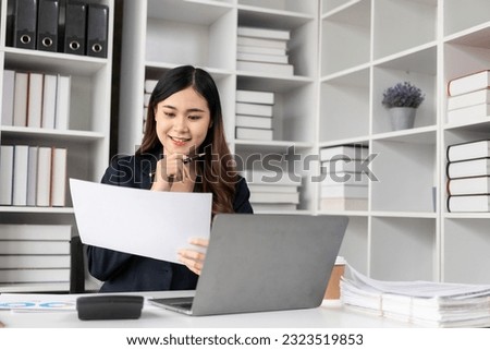 Asian female accountant doing payroll of company employees with statistics and analytical research concept with financial graph working on laptop.