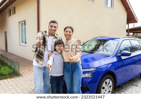 Joyful black family, finger pointing class, posing while standing next to a luxury car outdoors outside the house, smiling at the camera. Car leasing and ownership