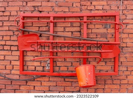 Red brick wall with a red paint bucket and a shovel in the foreground