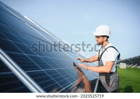 Side view of male worker installing solar modules and support structures of photovoltaic solar array. Electrician wearing safety helmet while working with solar panel. Concept of sun energy. Royalty-Free Stock Photo #2323525719