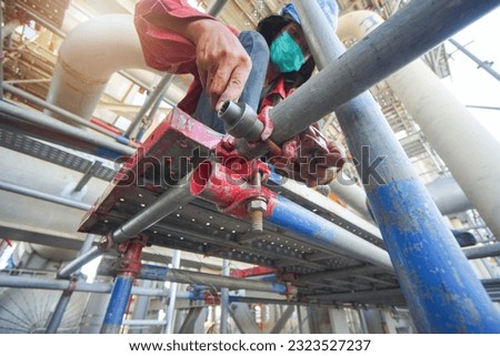 Worker with wrench in his hand builds iron scaffold on construction site,scaffolding Royalty-Free Stock Photo #2323527237