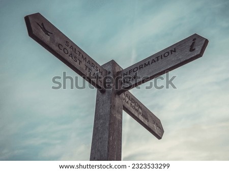A wooden signpost against a blue clouded sky