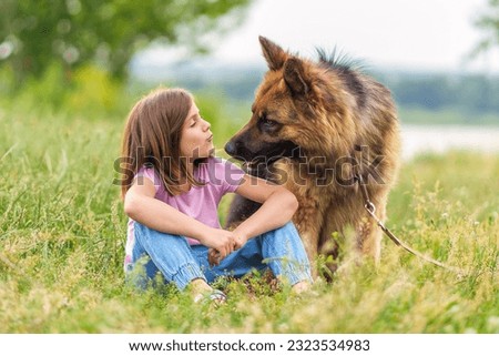 Cute little girl kissing shepherd dog sitting in the grass in the park in summer. High quality photo, blurred background