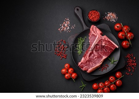 Raw juicy beef t-bone steak with salt, spices and herbs on a textured concrete background Royalty-Free Stock Photo #2323539809