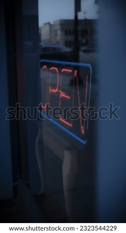A vertical shot of a neon red open sign behind a cafe window