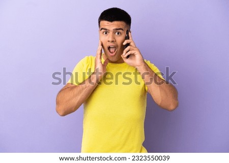 Young handsome man using mobile phone over isolated purple background with surprise and shocked facial expression