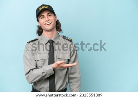 Young safeguard man isolated on blue background presenting an idea while looking smiling towards