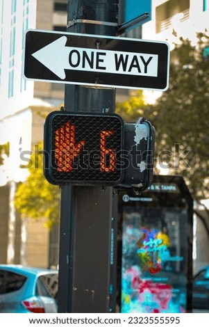 A vertical closeup of the one-way sign on the street with a red light on.