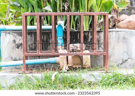 Small water pump and motor broken damaged old rusty pipes. Installed next to pond in the park. There is plastic water pipe to pump water. surrounded by weeds that. Electric leakage safety concept.