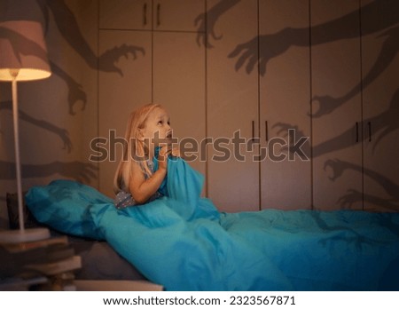 Fear, shadow and monster with a girl in bed at night feeling afraid or scared of the dark. Kids, horror or nightmare with a young female child sitting alone in a dark, spooky and creepy bedroom Royalty-Free Stock Photo #2323567871