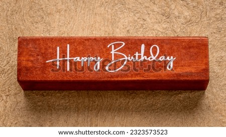 Happy Birthday text on wooden block against handmade bark paper in earth tones, greeting concept
