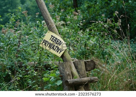 An open wooden gate pole with a sign in Polish in the middle of a forest\nTranslation - private terrain