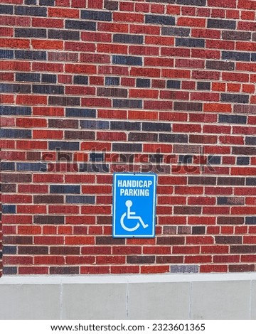 A handicap parking sing on a red and black brick wall