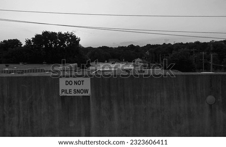 A black and white shot of a "Do not pile snow here" street sign on a wall with nature in the background