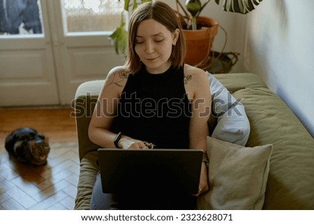 Smiling woman using laptop for online learning or watching movie while lying on sofa at home