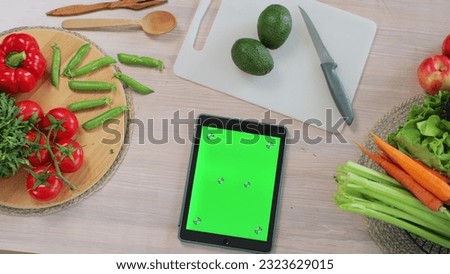 Tablet with green screen in the kitchen on table with fresh vegetables and fruit. Application for cooking. Healthy food concept.