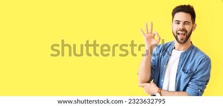 Happy young man showing OK on yellow background with space for text Royalty-Free Stock Photo #2323632795