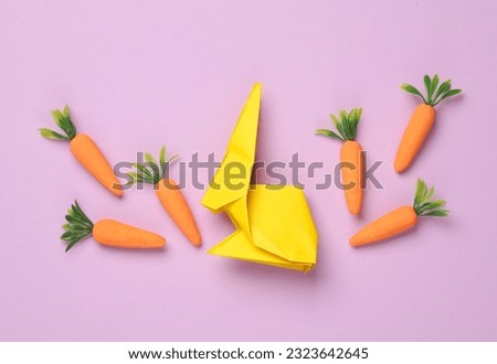 Origami rabbit with a carrot on a purple pastel background. Easter concept