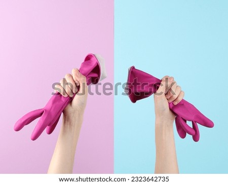 Hands holding pink rubber gloves for cleaning on a blue-pink pastel background