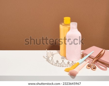 A sparkling jewelry tiara with expensive stones, a roller facial massager, a pink wallet for money and business cards, makeup brushes and cleansing gels. Copy space for text.